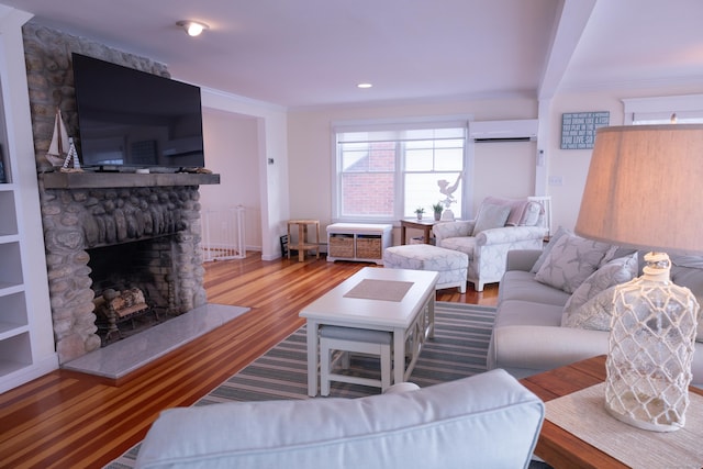 living room with a wall mounted air conditioner, wood-type flooring, a stone fireplace, and ornamental molding