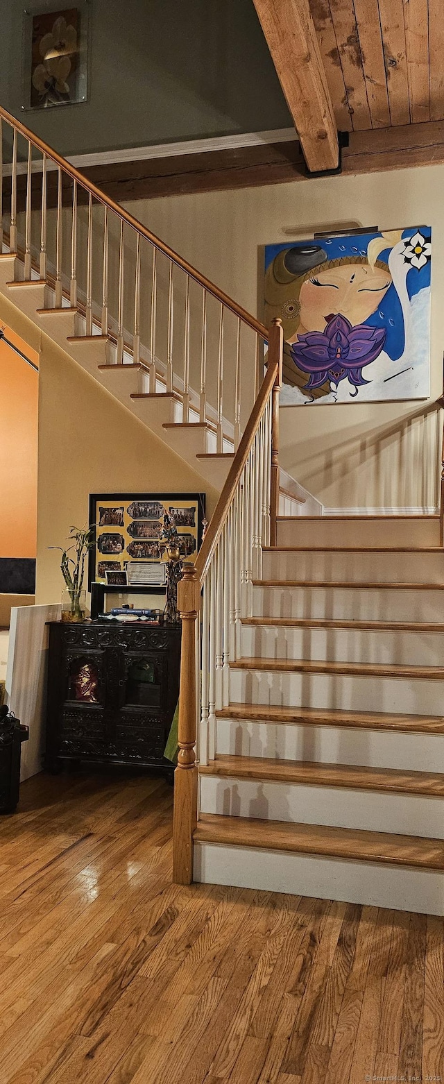 stairs with beam ceiling, hardwood / wood-style floors, and wood ceiling