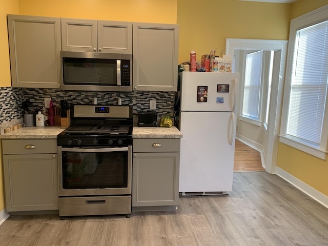 kitchen featuring gray cabinetry, decorative backsplash, light wood-type flooring, and stainless steel appliances