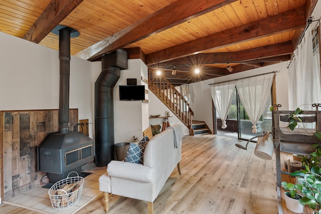 living room with beamed ceiling, light hardwood / wood-style floors, a wood stove, and wooden ceiling