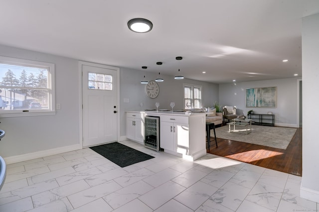 interior space featuring kitchen peninsula, wine cooler, light wood-type flooring, decorative light fixtures, and white cabinetry