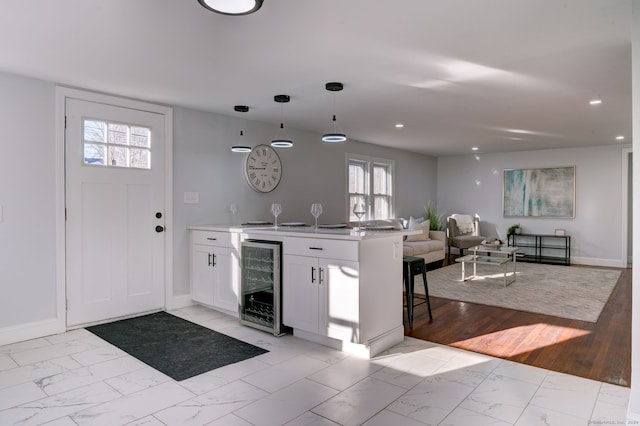 kitchen featuring kitchen peninsula, decorative light fixtures, light hardwood / wood-style flooring, white cabinets, and wine cooler