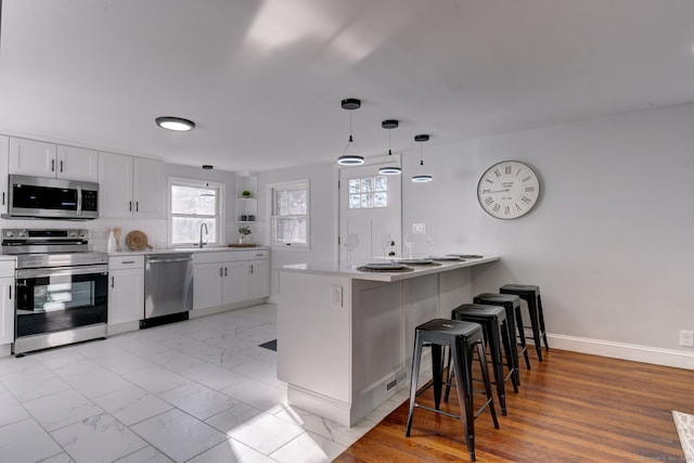 kitchen with white cabinets, appliances with stainless steel finishes, kitchen peninsula, and pendant lighting