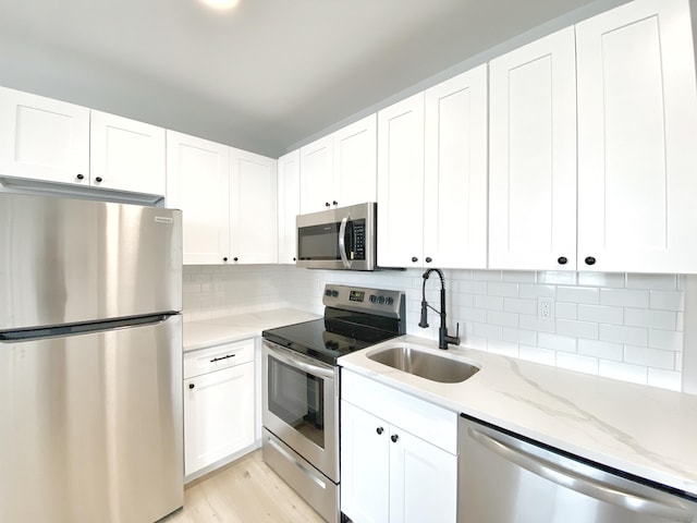 kitchen featuring white cabinetry, sink, backsplash, light stone counters, and stainless steel appliances