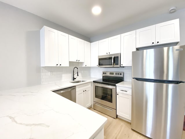 kitchen with appliances with stainless steel finishes, sink, white cabinets, backsplash, and light stone counters