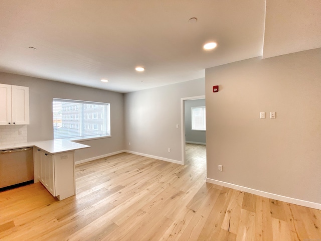 kitchen with tasteful backsplash, white cabinets, stainless steel dishwasher, light hardwood / wood-style floors, and kitchen peninsula