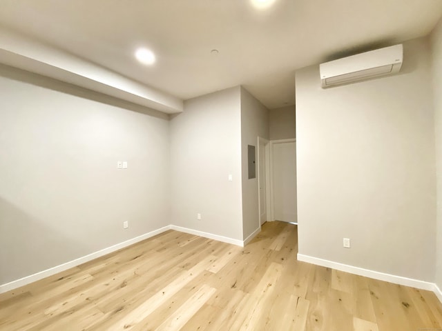 basement featuring an AC wall unit, electric panel, and light hardwood / wood-style flooring