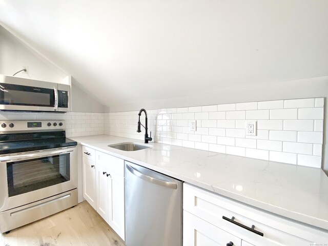 kitchen featuring appliances with stainless steel finishes, lofted ceiling, sink, white cabinets, and decorative backsplash