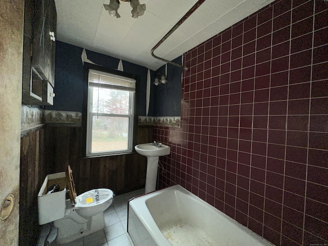 bathroom with toilet, tiled shower / bath combo, tile patterned floors, and tile walls