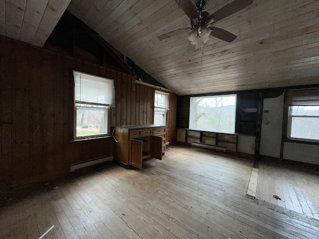 spare room with baseboard heating, wood walls, light hardwood / wood-style floors, and vaulted ceiling