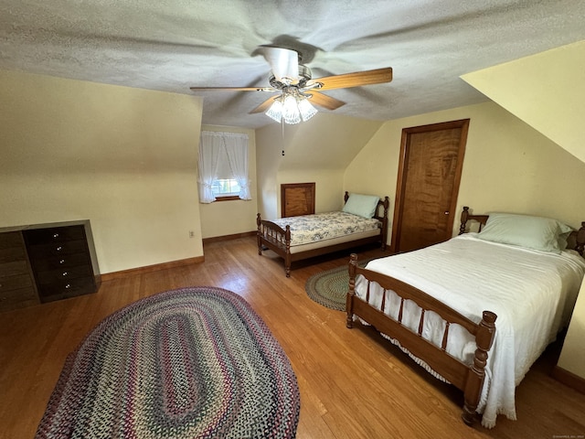 bedroom with ceiling fan, vaulted ceiling, a textured ceiling, and light hardwood / wood-style flooring