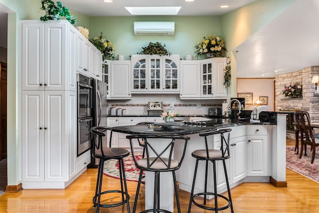 kitchen featuring white cabinets, kitchen peninsula, a wall unit AC, and a skylight