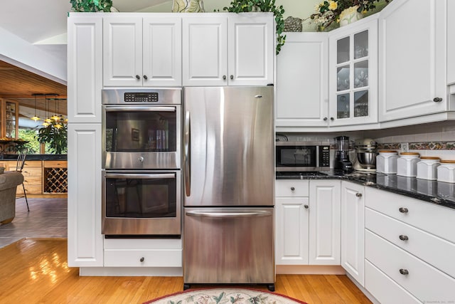 kitchen with white cabinets, stainless steel appliances, dark stone counters, and light hardwood / wood-style flooring