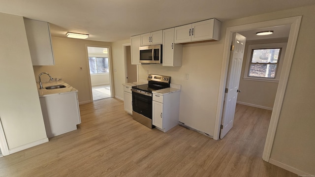 kitchen featuring appliances with stainless steel finishes, light wood-type flooring, light stone counters, sink, and white cabinetry