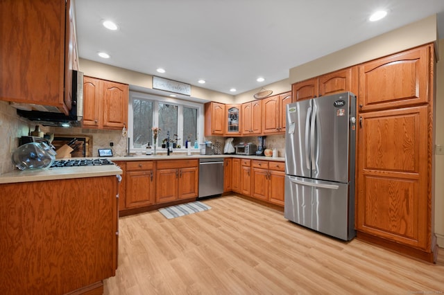 kitchen featuring sink, light wood-type flooring, backsplash, and appliances with stainless steel finishes