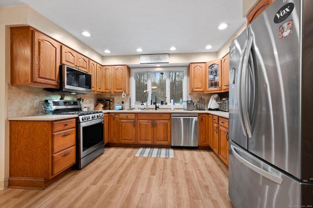 kitchen with appliances with stainless steel finishes, light wood-type flooring, tasteful backsplash, and sink