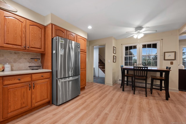 kitchen with ceiling fan, baseboard heating, backsplash, stainless steel fridge, and light hardwood / wood-style floors