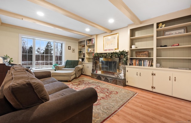 living room featuring a stone fireplace, beamed ceiling, and light wood-type flooring