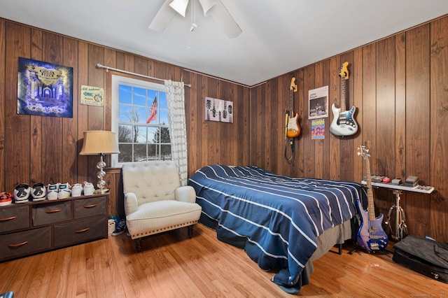 bedroom featuring light hardwood / wood-style flooring, ceiling fan, and wood walls