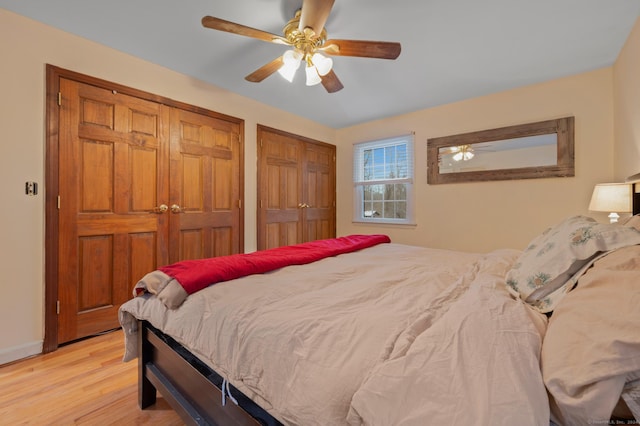 bedroom featuring ceiling fan, two closets, and light hardwood / wood-style flooring