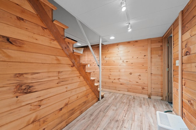 basement featuring rail lighting, light hardwood / wood-style flooring, and wood walls