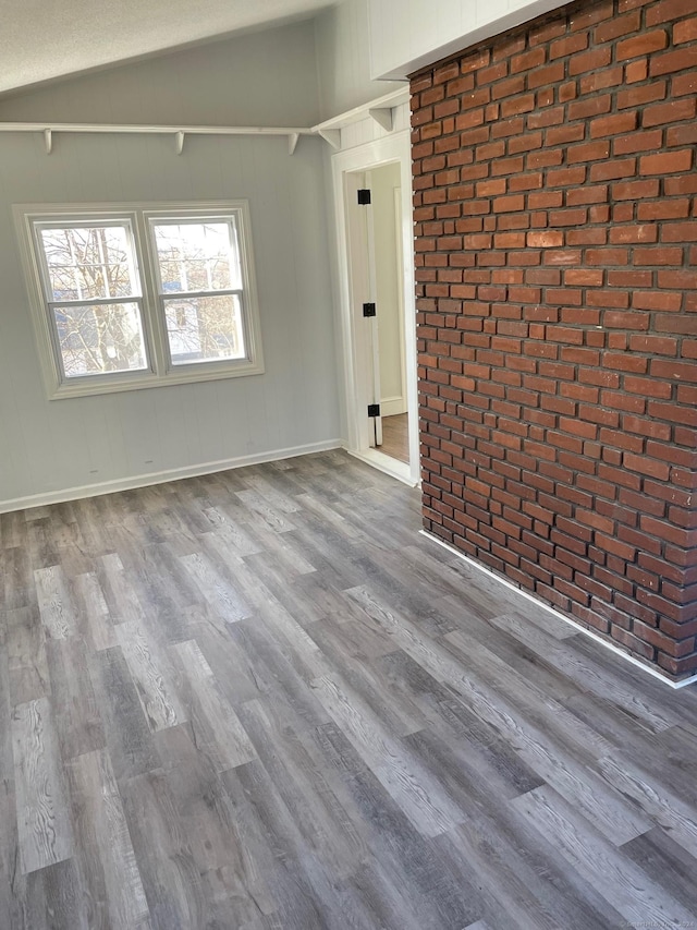 spare room with brick wall, vaulted ceiling, and hardwood / wood-style flooring