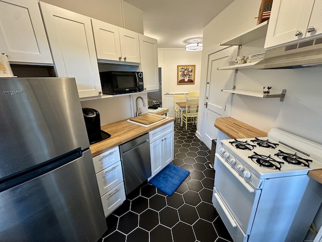 kitchen with wood counters, white cabinets, sink, dark tile patterned floors, and appliances with stainless steel finishes