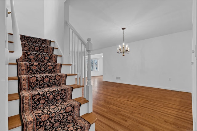 stairway with wood-type flooring and a notable chandelier