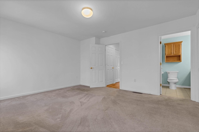 unfurnished bedroom with light carpet, ensuite bath, and a closet