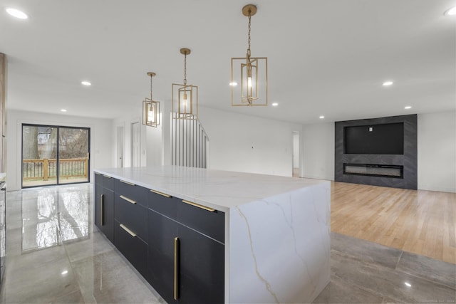 kitchen featuring a spacious island, light stone countertops, a high end fireplace, pendant lighting, and a notable chandelier