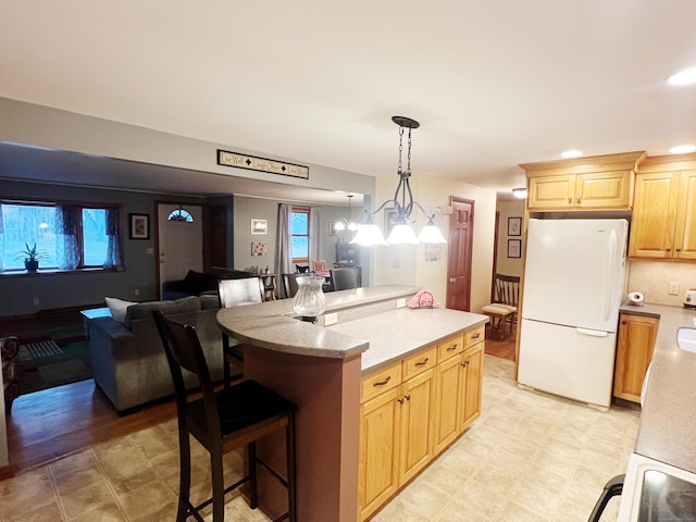 kitchen with light brown cabinetry, a chandelier, decorative light fixtures, and white refrigerator