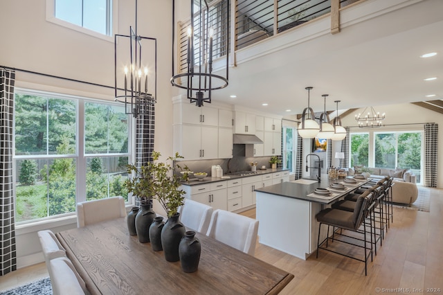 kitchen with dark countertops, light wood-style floors, white cabinetry, a sink, and under cabinet range hood