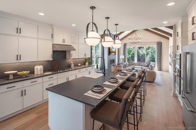 kitchen featuring dark countertops, lofted ceiling with beams, decorative backsplash, a sink, and under cabinet range hood