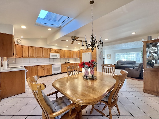 dining room featuring vaulted ceiling with skylight, ceiling fan with notable chandelier, light tile patterned flooring, and sink