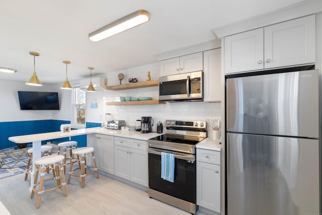 kitchen with pendant lighting, light wood-type flooring, stainless steel appliances, and white cabinetry