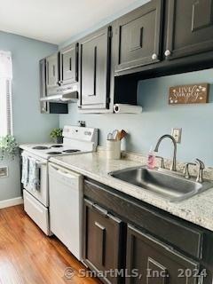 kitchen with sink, light stone counters, extractor fan, white appliances, and hardwood / wood-style flooring