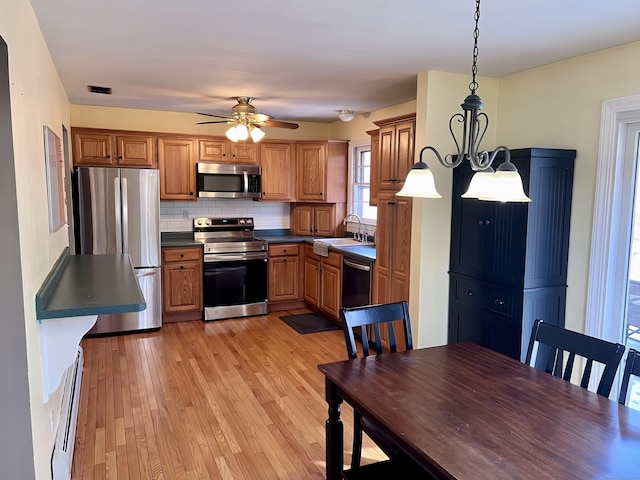 kitchen featuring sink, light hardwood / wood-style flooring, hanging light fixtures, stainless steel appliances, and decorative backsplash