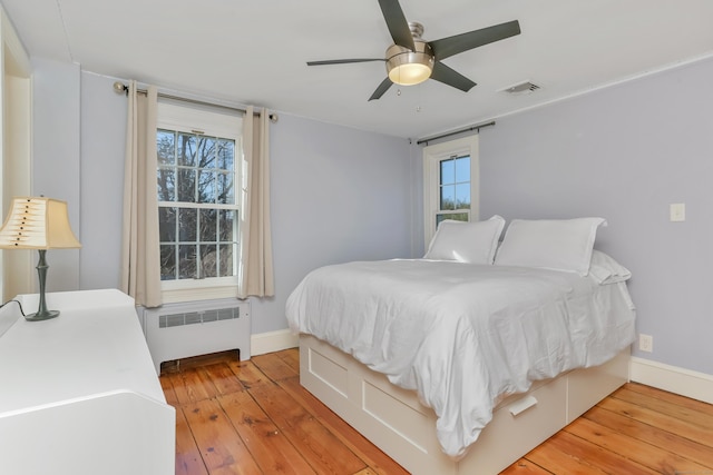 bedroom with baseboards, visible vents, hardwood / wood-style floors, and radiator heating unit