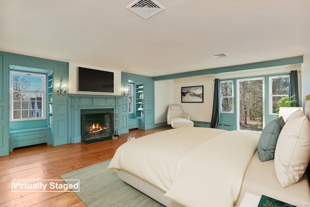 bedroom featuring a baseboard radiator, a warm lit fireplace, visible vents, and hardwood / wood-style floors