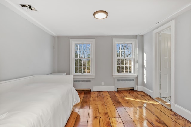 bedroom featuring light wood finished floors, radiator heating unit, visible vents, and baseboards