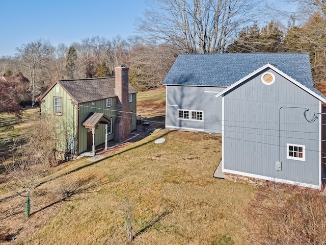 exterior space with a shingled roof, a chimney, a lawn, and an outbuilding