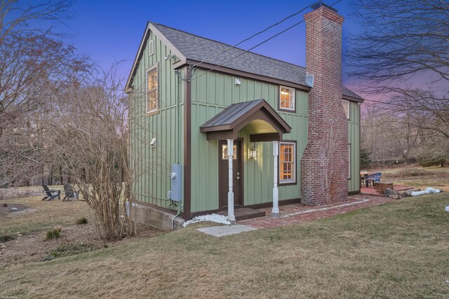 view of front of home with board and batten siding, roof with shingles, a chimney, and a front lawn