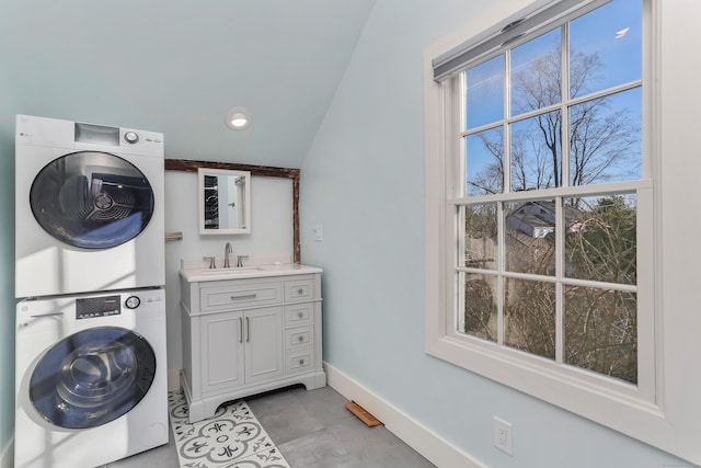 washroom with a sink, cabinet space, baseboards, and stacked washer / drying machine