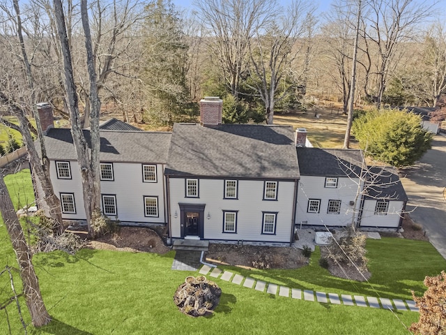 view of front of property featuring a front yard, roof with shingles, and a chimney