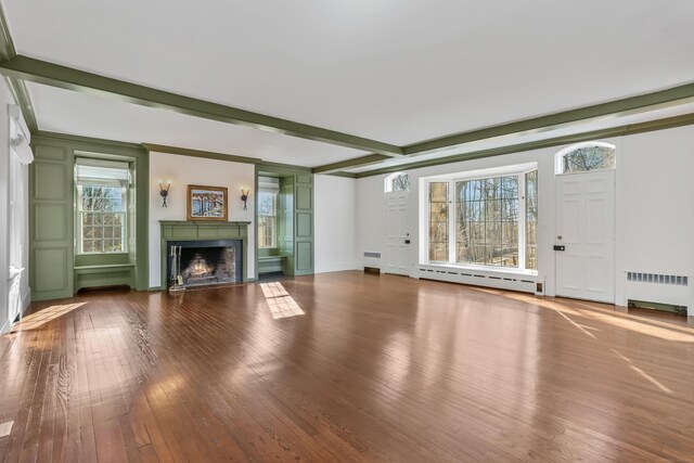 unfurnished living room with beam ceiling, radiator, a baseboard heating unit, a warm lit fireplace, and hardwood / wood-style flooring