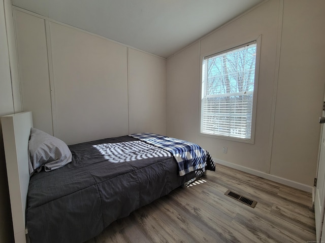 bedroom featuring lofted ceiling, light wood-style floors, visible vents, and a decorative wall