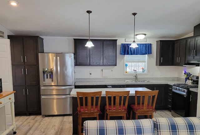 kitchen featuring light wood-style flooring, under cabinet range hood, stainless steel appliances, a sink, and decorative light fixtures