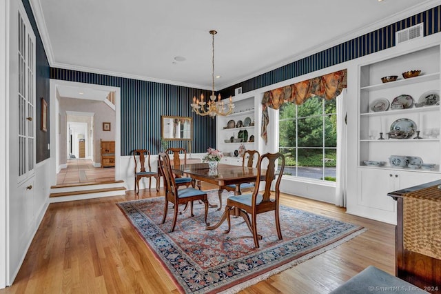 dining space with built in shelves, a chandelier, ornamental molding, and light wood-type flooring