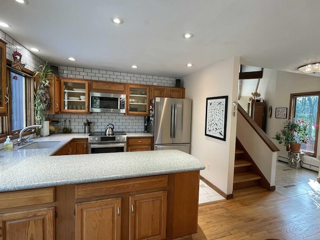 kitchen with sink, backsplash, kitchen peninsula, appliances with stainless steel finishes, and light wood-type flooring