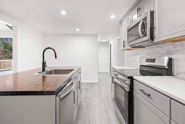 kitchen featuring appliances with stainless steel finishes, sink, a center island with sink, light hardwood / wood-style flooring, and butcher block countertops